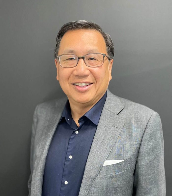 Smiling man wearing glasses and a gray blazer over a navy shirt.
